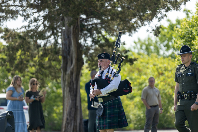 A bagpiper leads a procession of conservation officers to the memorial as a crowd watches
