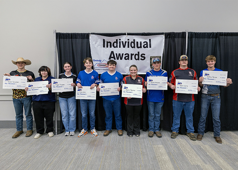 Nine Students holding up paper certificates in front of a sign that reads individual awards