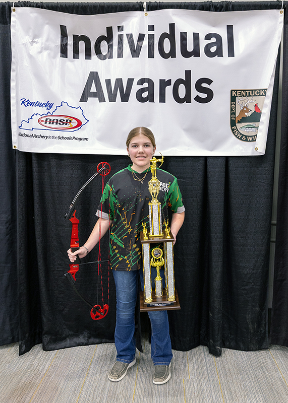 A student holding up large trophy and a genesis bow in front of a sign that reads individual awards