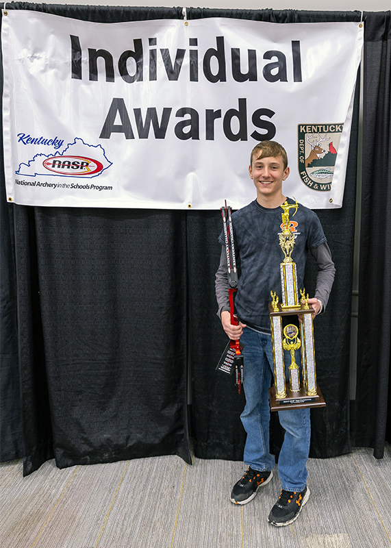 A student holding up large trophy and a genesis bow in front of a sign that reads individual awards