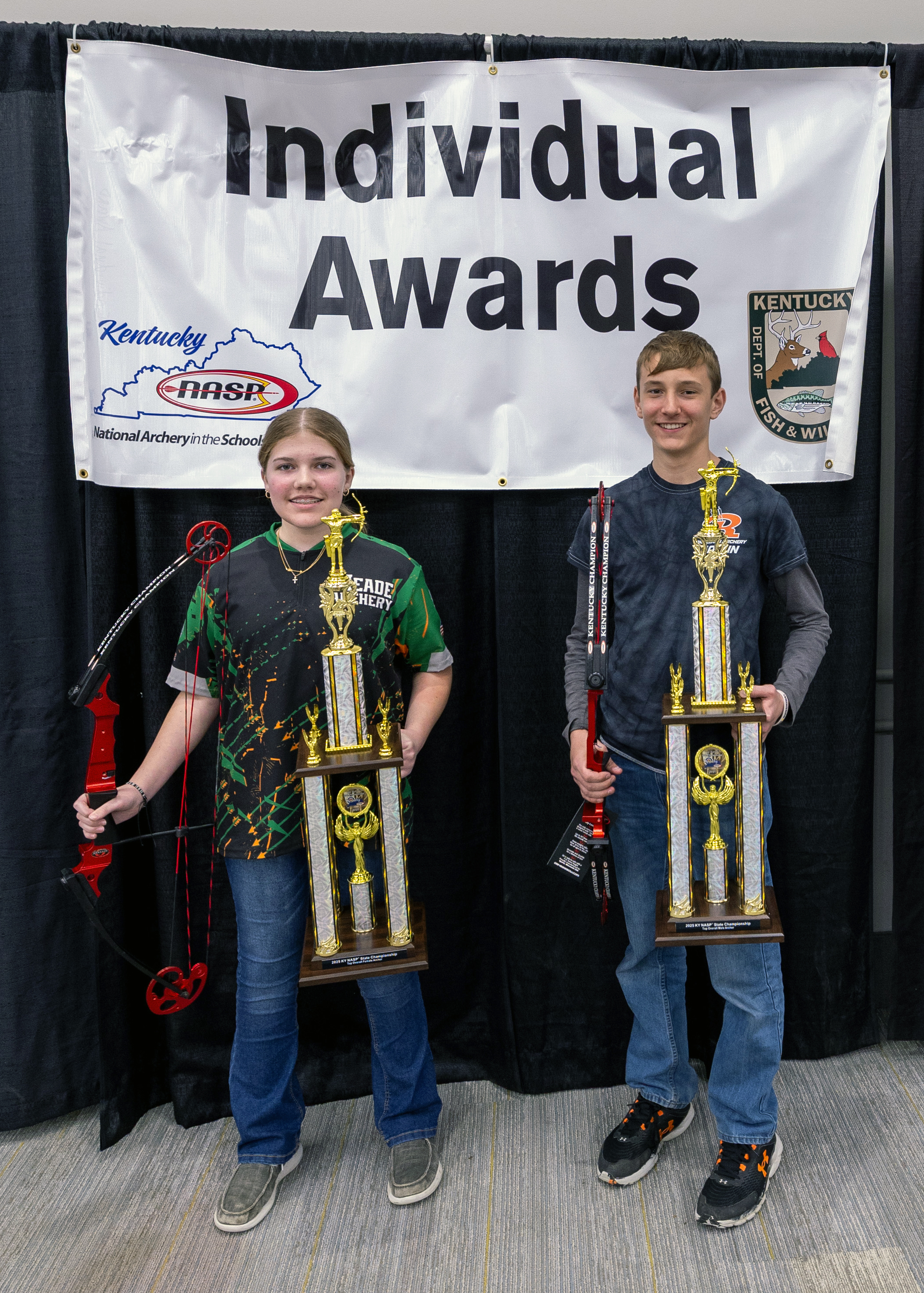 Two Students holding up large trophies in front of a sign that reads individual awards
