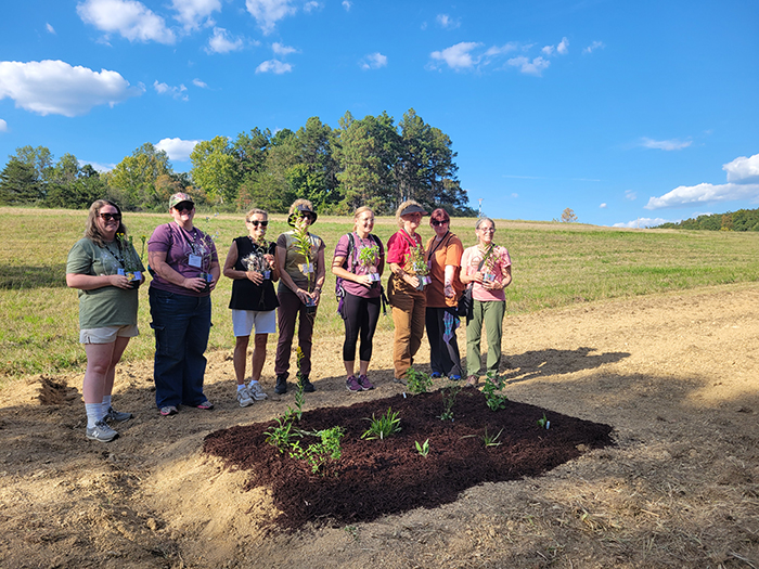 a group of eight women holding up plants next to an planted garden