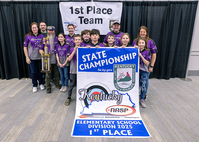 A group of eight students and six adults in front of a sign that reads 1st place team. they are also holding a banner that reads elementary schoool division 1st place