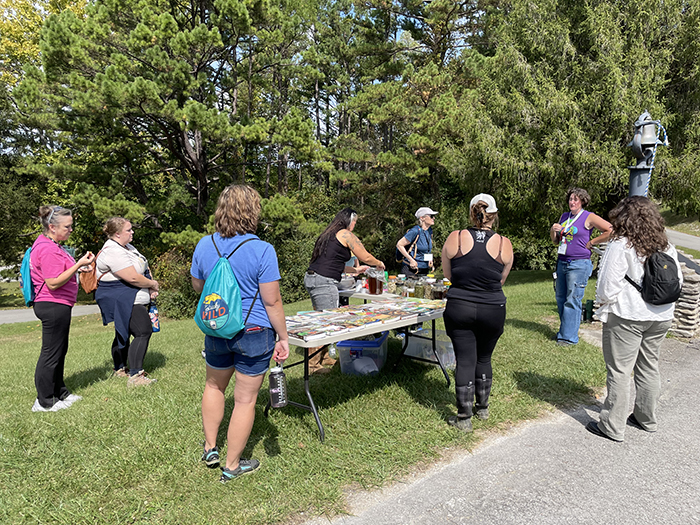 a group of people standing around a display table listening to a speaking instructor