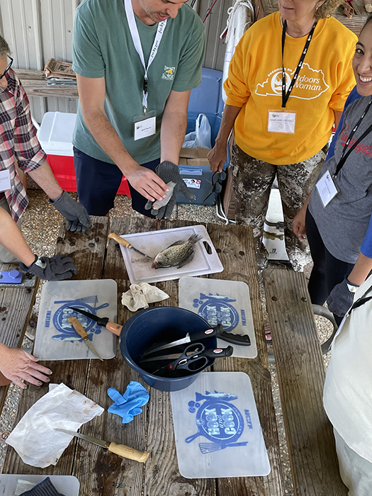 people around a table watching an instructor show how to process a fish.