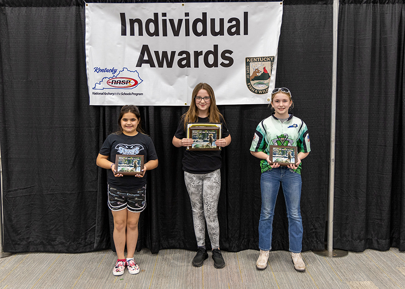 Three students holding up award plaques in front of a sign that reads individual awards