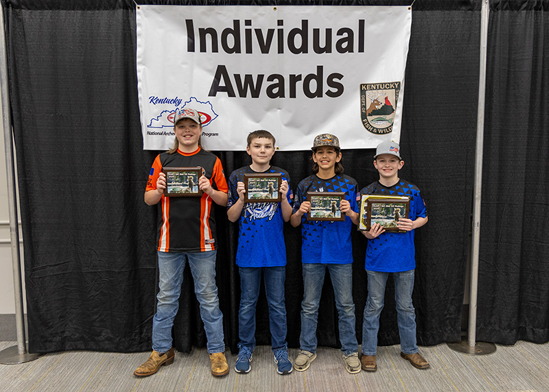 four students holding up award plaques in front of a sign that reads individual awards