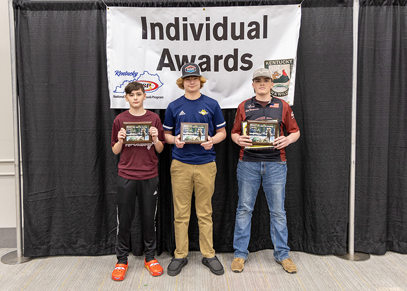 three students holding up award plaques in front of a sign that reads individual awards