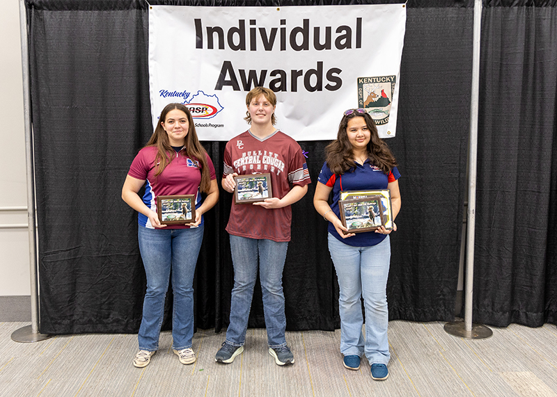 three students holding up award plaques in front of a sign that reads individual awards