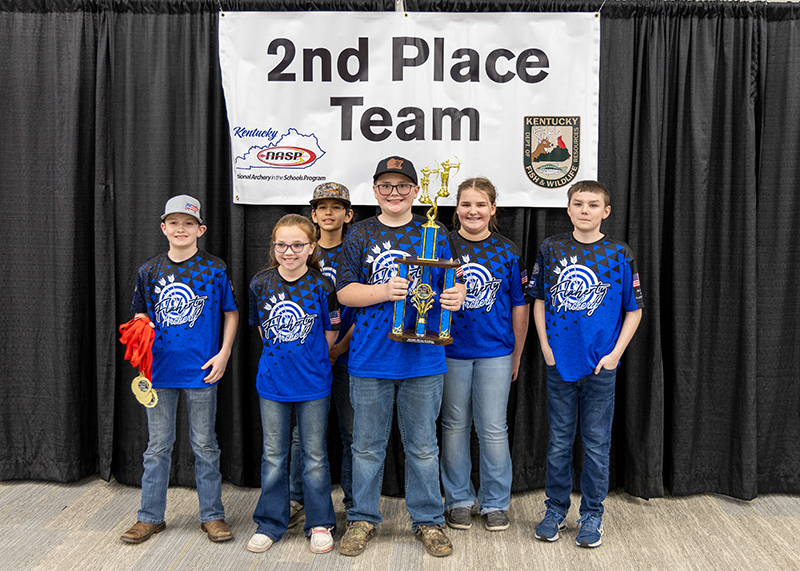 A group of students are standing in front of a sign that reads 2nd place team. the student in the center is holding up a large trophy