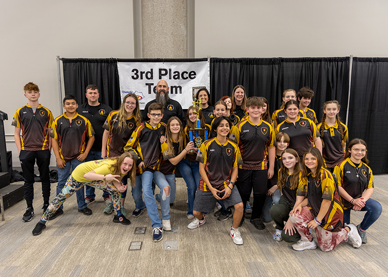 A group of students are standing in front of a sign that reads 3rd place team. the student in the center is holding up a large trophy