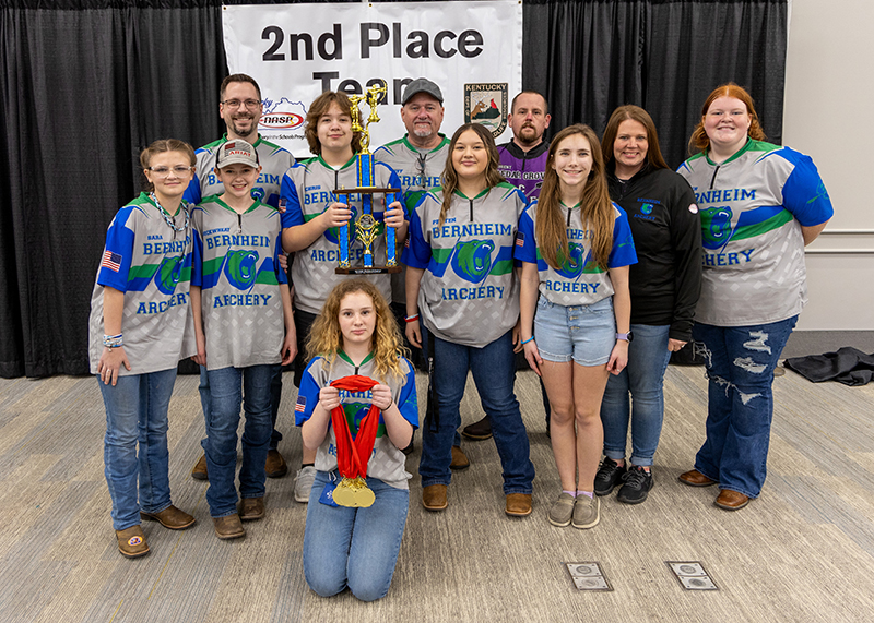 A group of students are standing in front of a sign that reads 2nd place team. the student in the center is holding up a large trophy