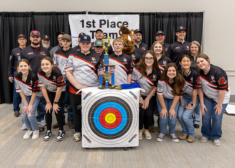 A group of students are standing in front of a sign that reads 1st place team. the student in the center is holding up a large trophy