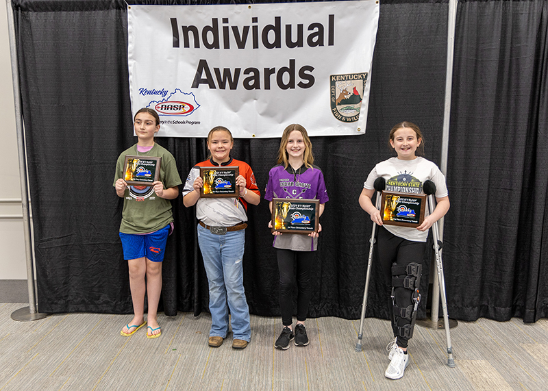 a group of 4 students for a group photograph holding plaques. A sign behind them reads Individual awards