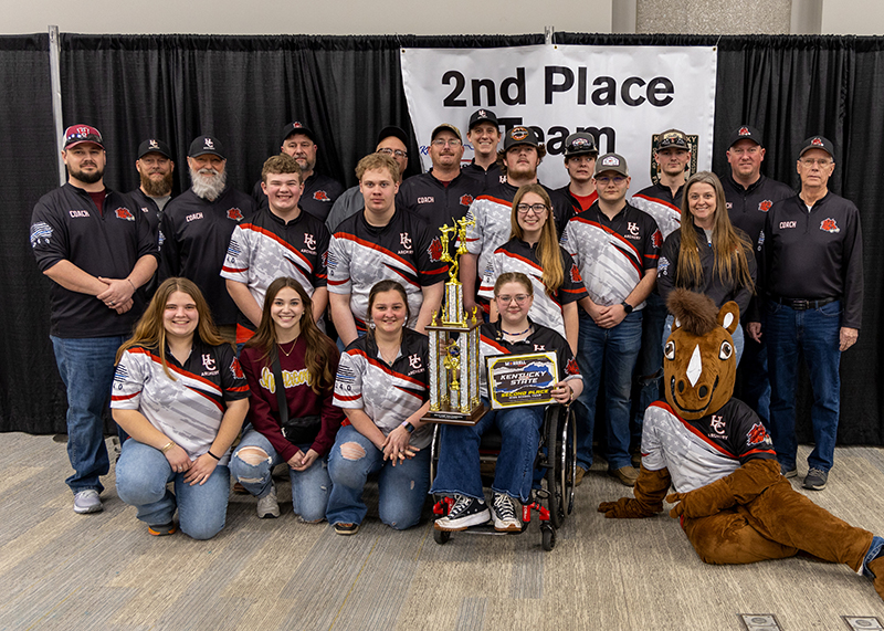 A group of students are standing in front of a sign that reads 2nd place team. the student in the center is holding up a large trophy