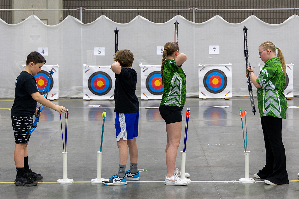 students standing in a line to shoot archery at targets