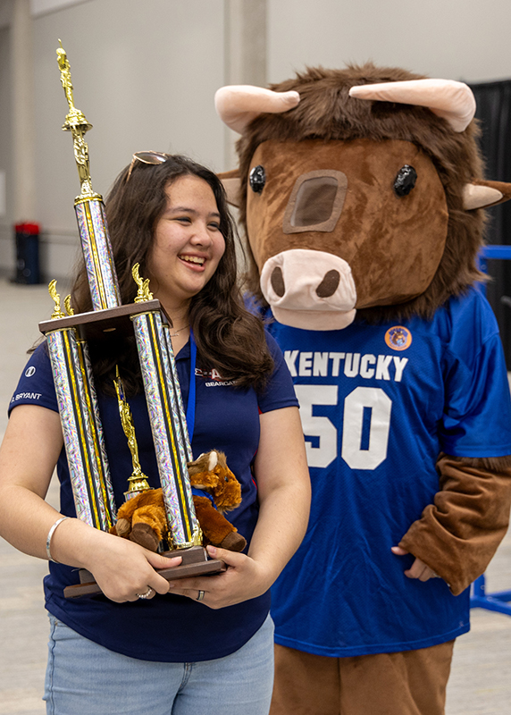 A student holding up a large trophy and standing next to a bull mascot