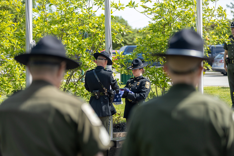 Two color guard officers are unfolding a flag in front of a flag pole as officers watch