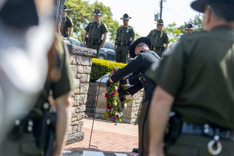 A conservation officer is hanging an floral wreath on a stand as Conservation Officers stand at attention around him