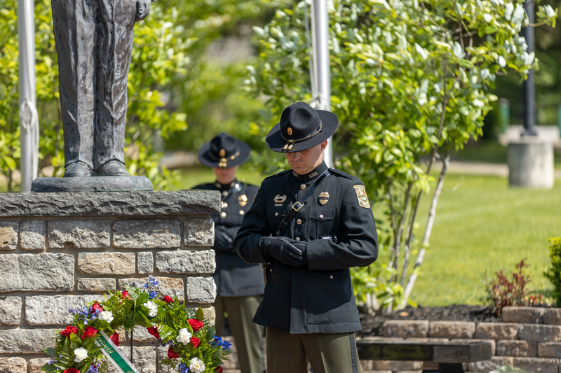 A Conservation Officer stands bowed in prayer next to a floral wreath in front of the memorial statue