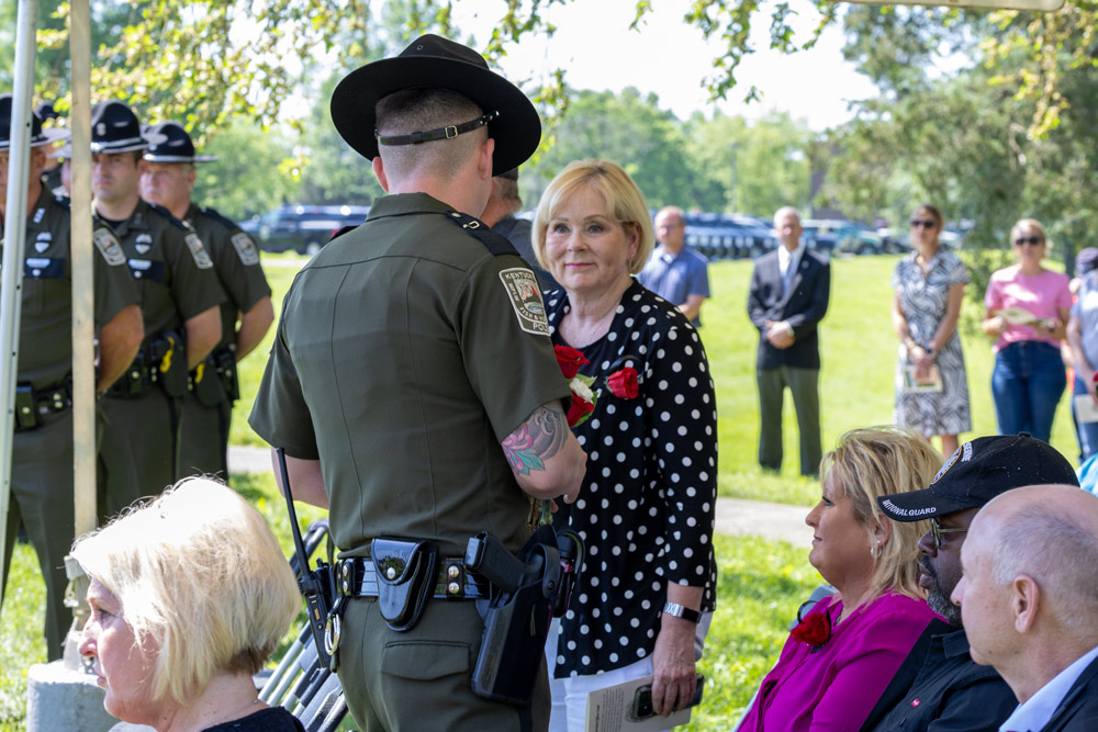 A man is speaking to a woman as people are seated under a tent