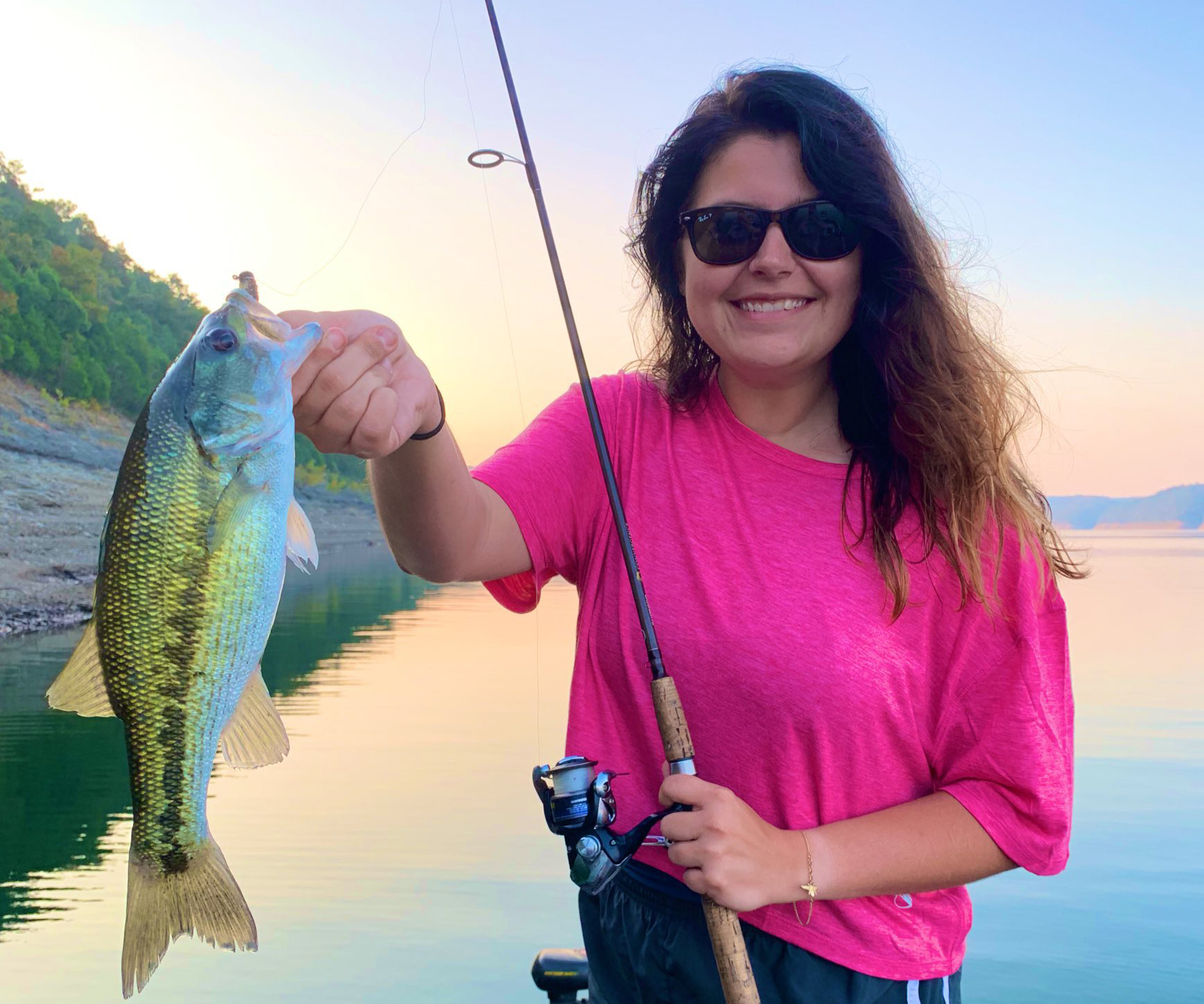 A woman is holding a large spotted bass and a fishing pole