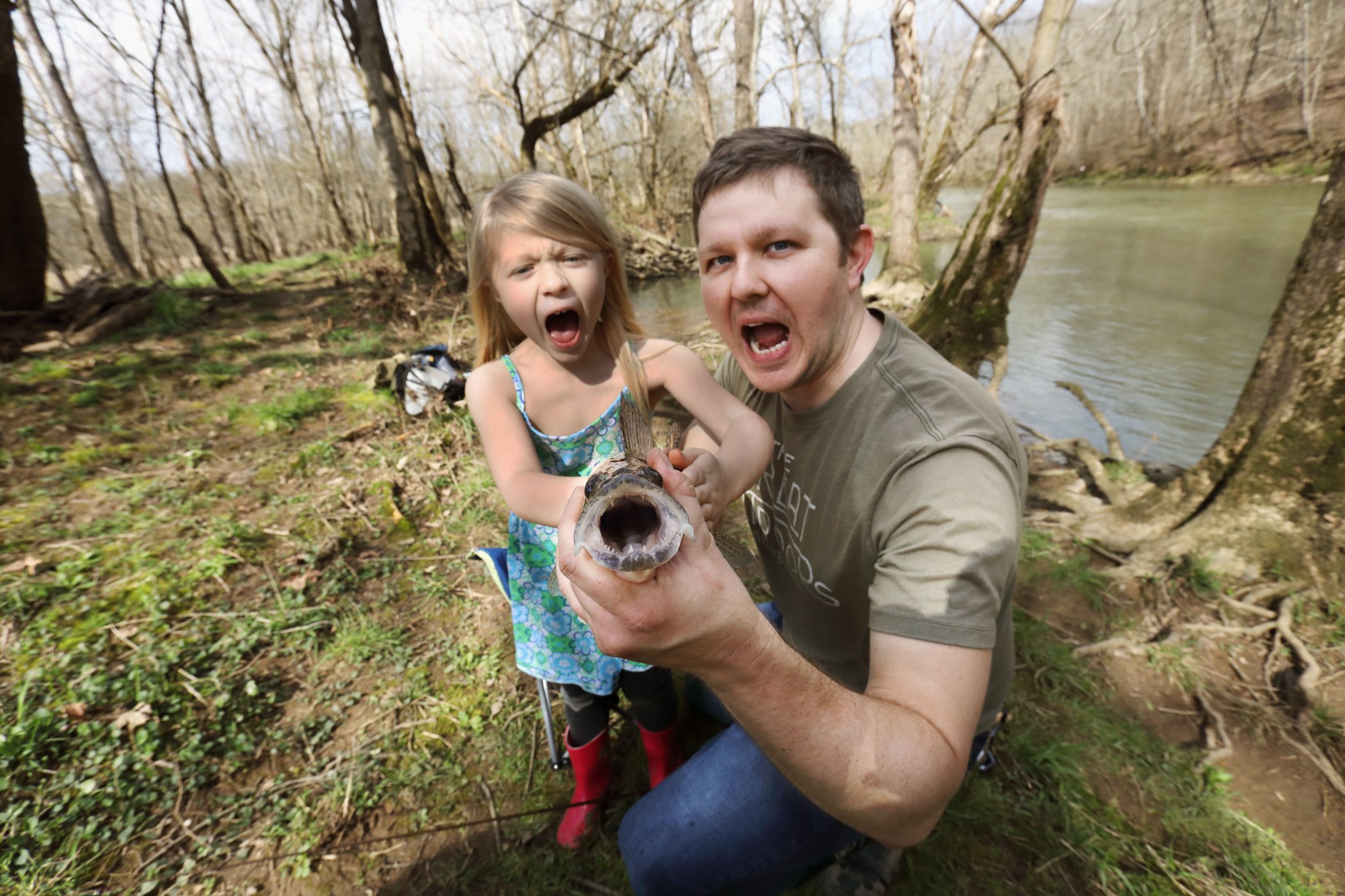 A little girl and a man are holding up a large fish and making open mouthed expressions
