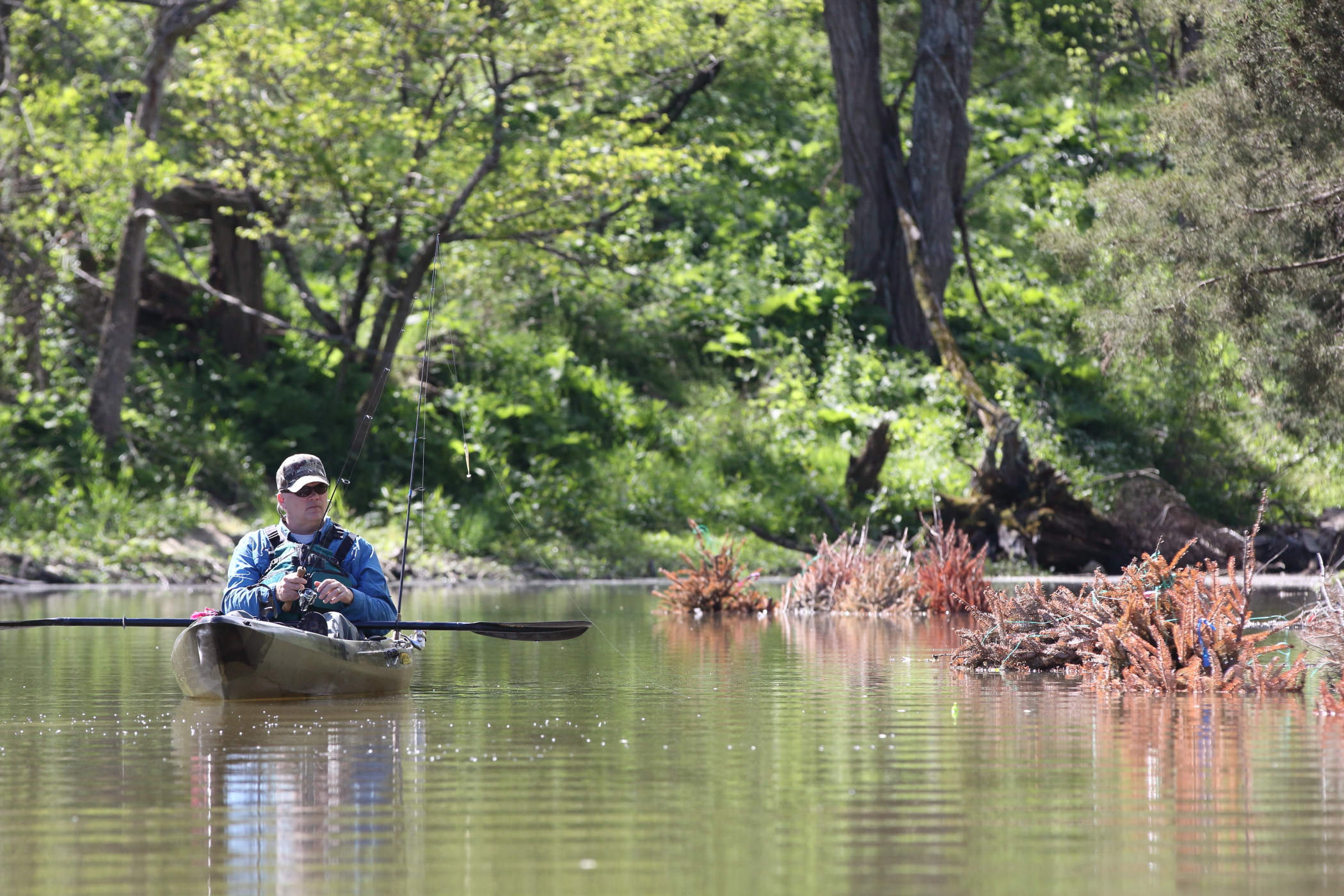A man is seated in a kayak casting a fishing line in a stream