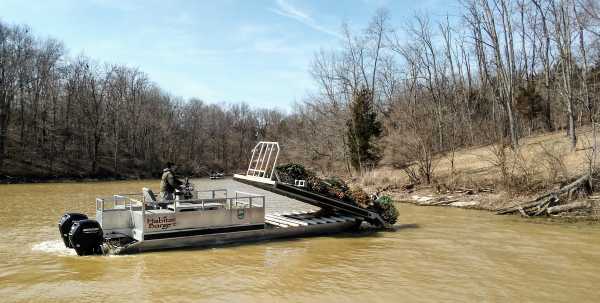 A boat is offloading trees of a barge into a river