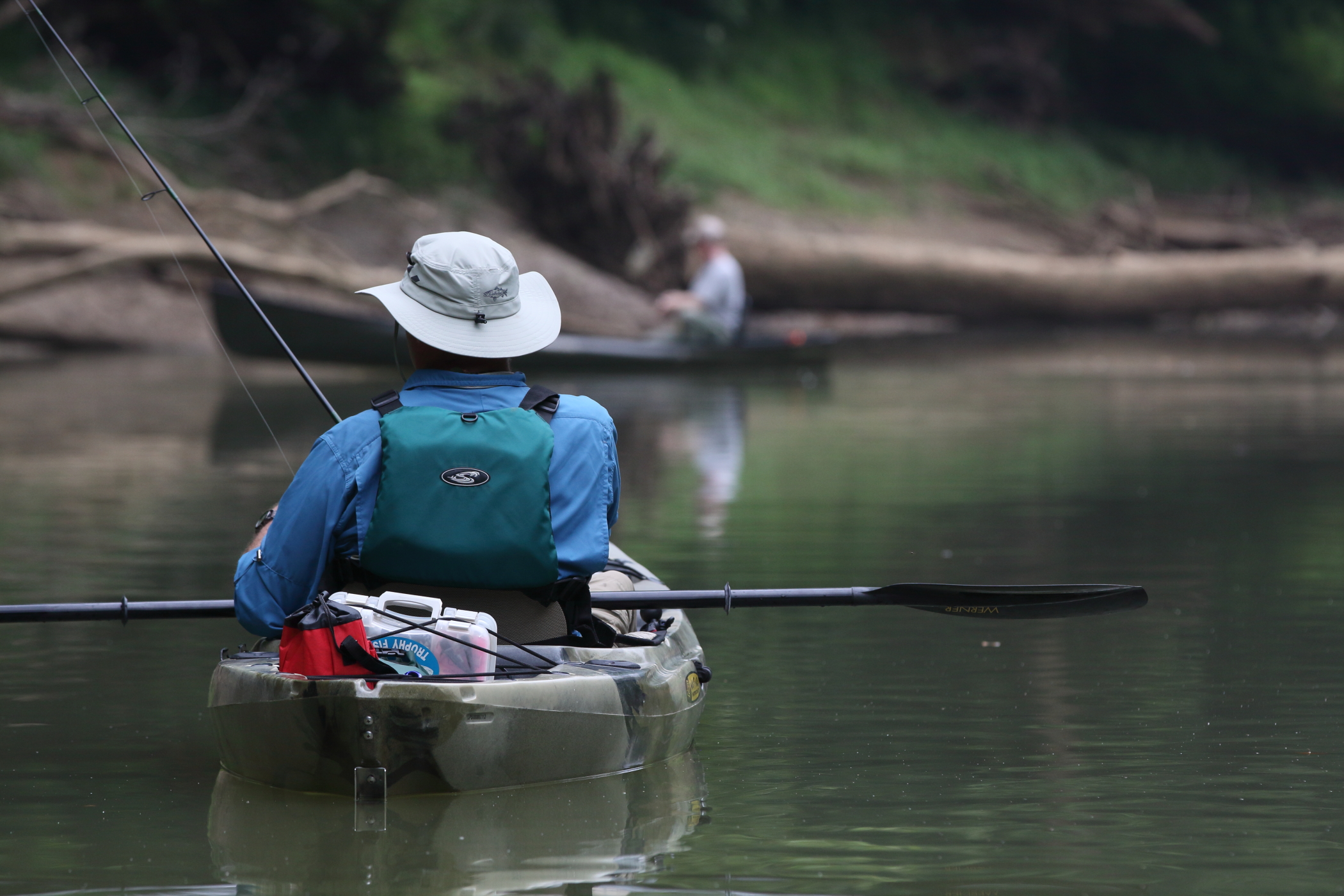 a man is fishing in a river while steering a kayak