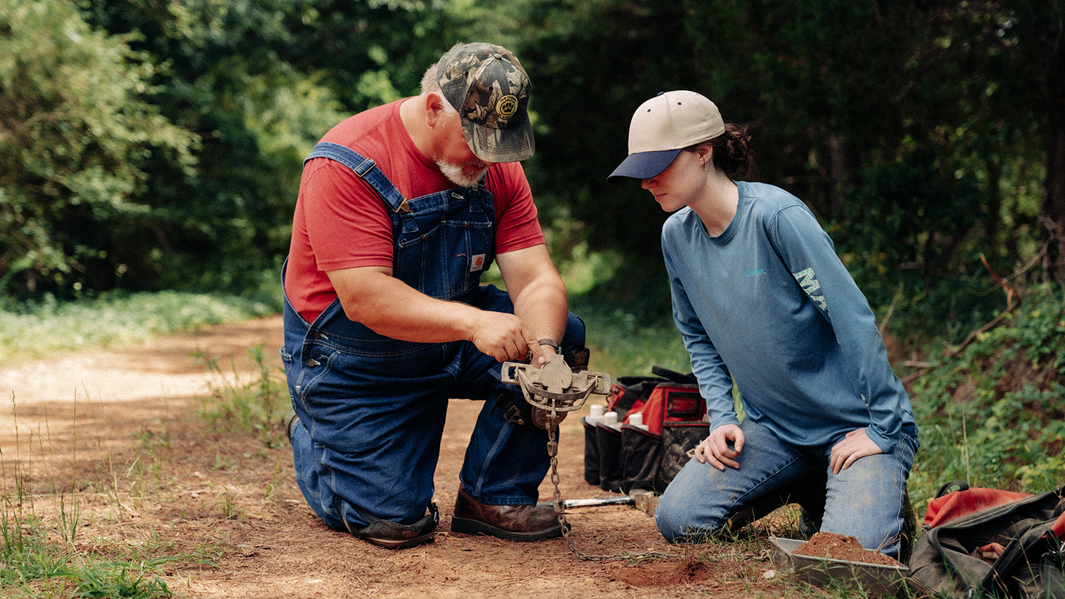 Mentor teaching youth to set a trap in a woods