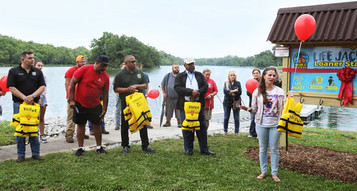 Group photograph showing a crowd of people standing and listening to a woman holding a lifejacket