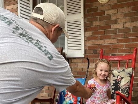 a man wearing a Fish and Wildlife shirt is handing suckers to a small child