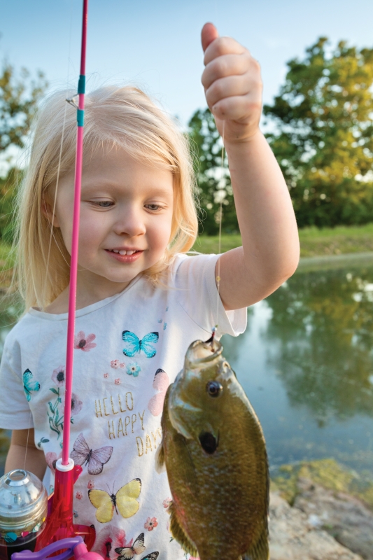 A little girl is holding up a large bluegill