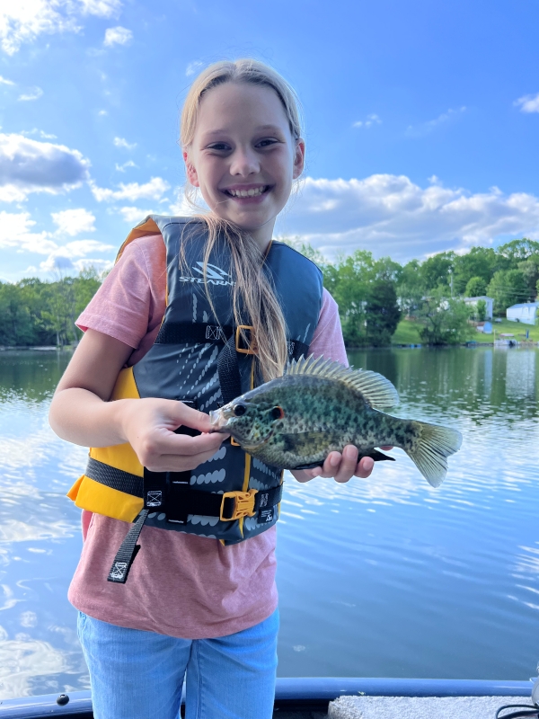 A girl is holding up a recently caught sunfish