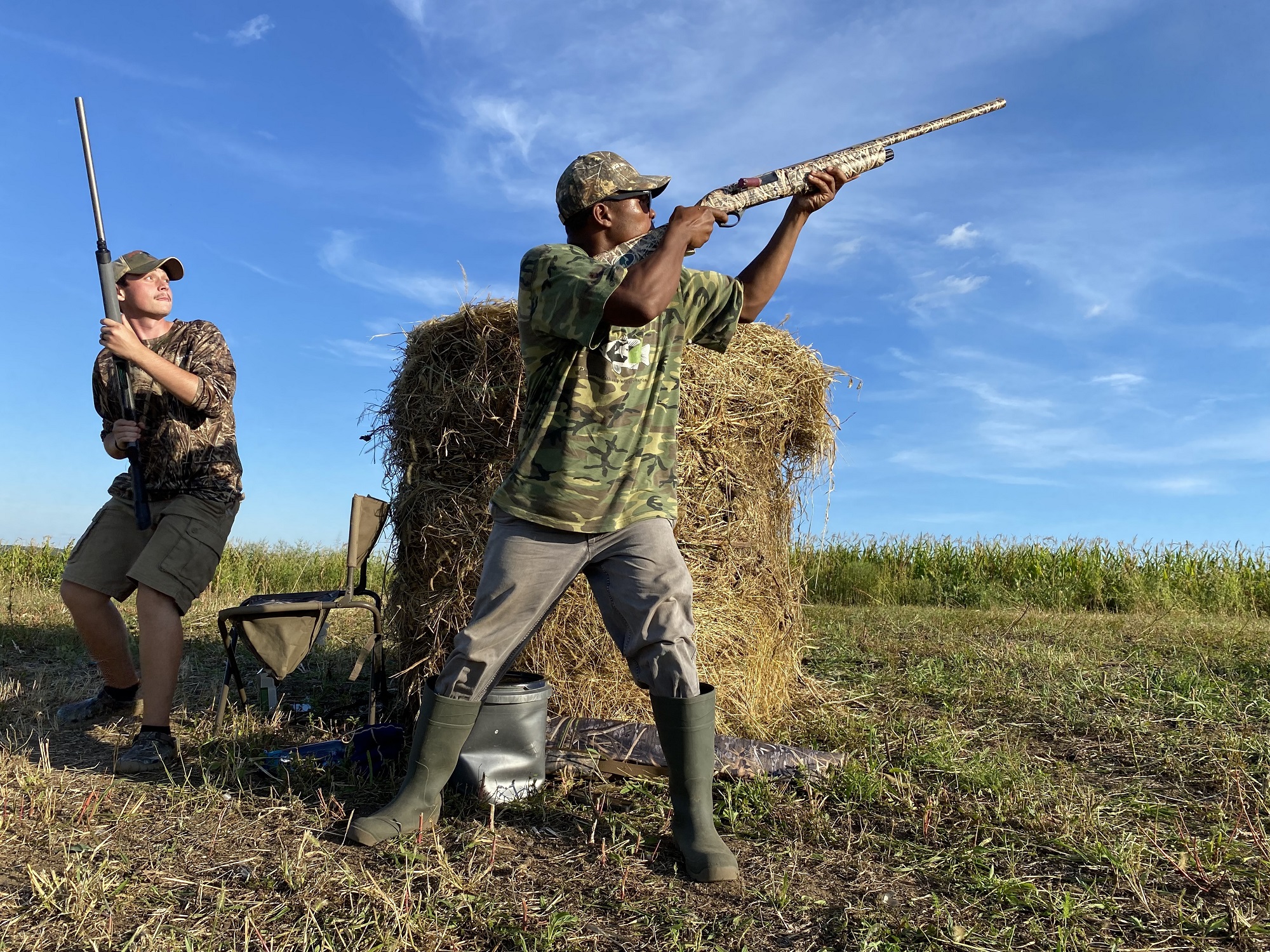 Dove hunter shooting at doves in a dove field with another hunter standing behind.