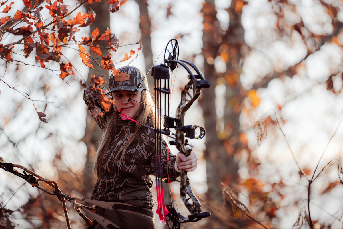 Female Archer shooting a compound bow in a treestand