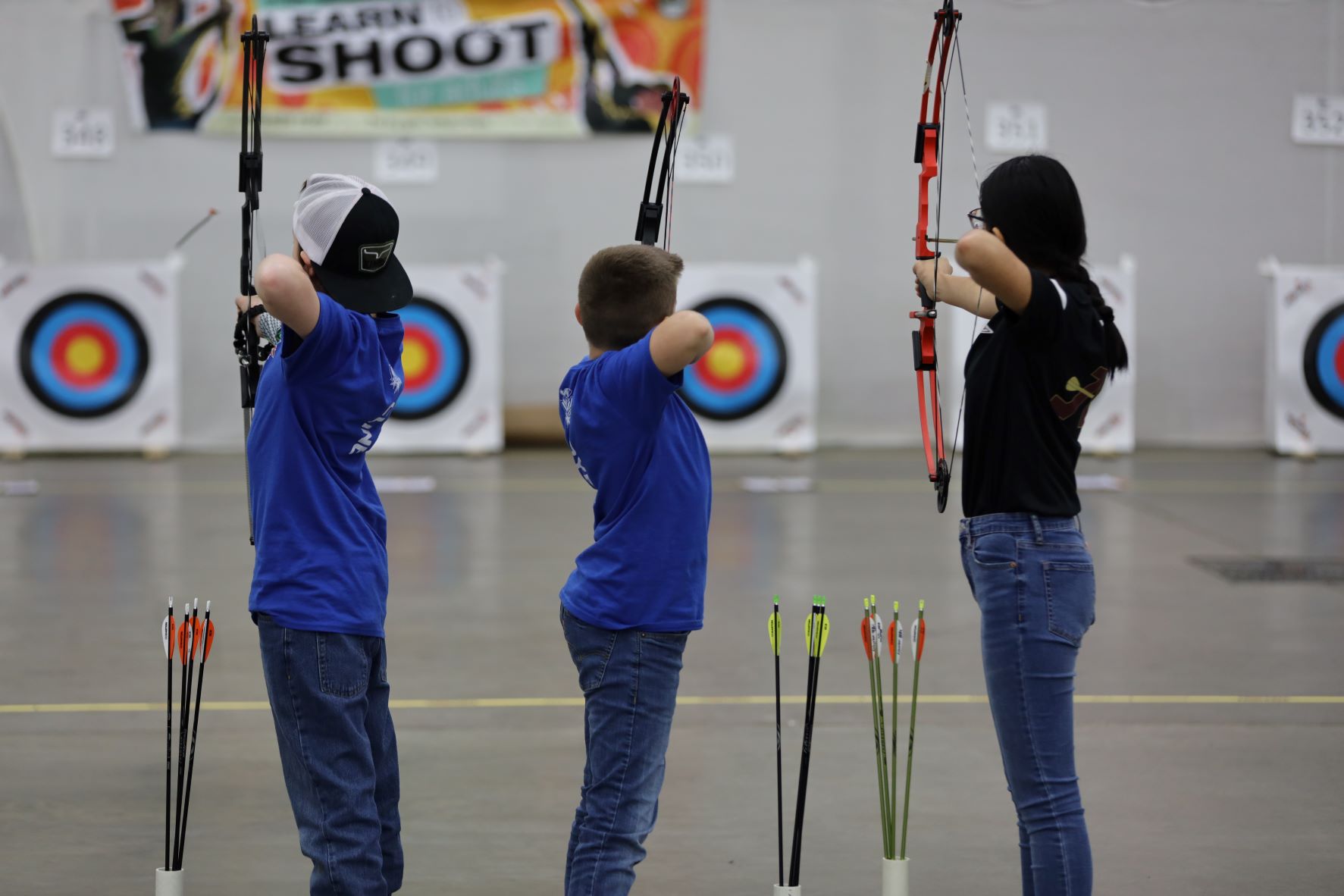 three students firing bows in an archery range