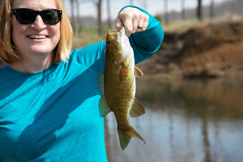 A woman is holding up a smallmouth bass